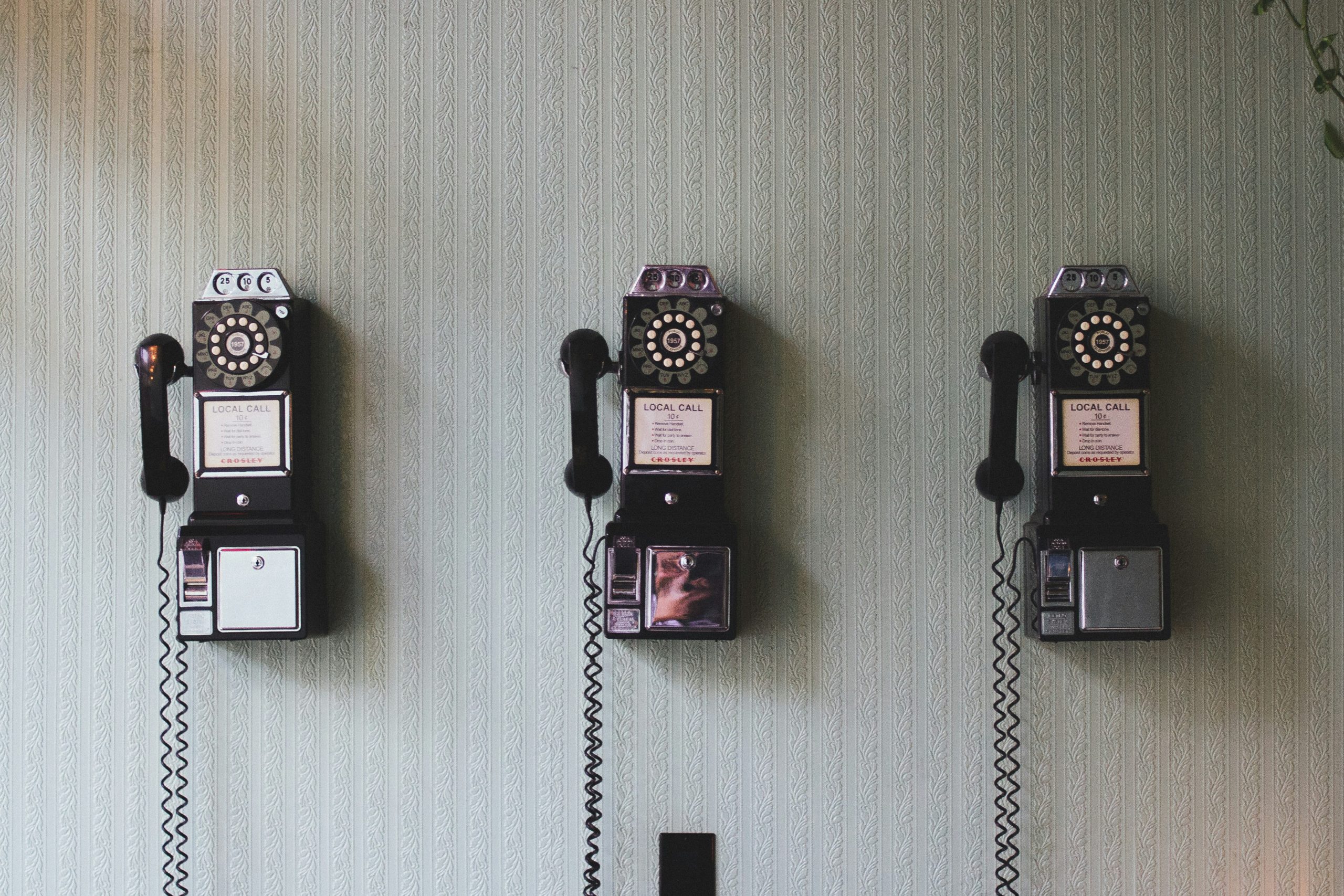 Three vintage wall-mounted pay phones from the mid-20th century.