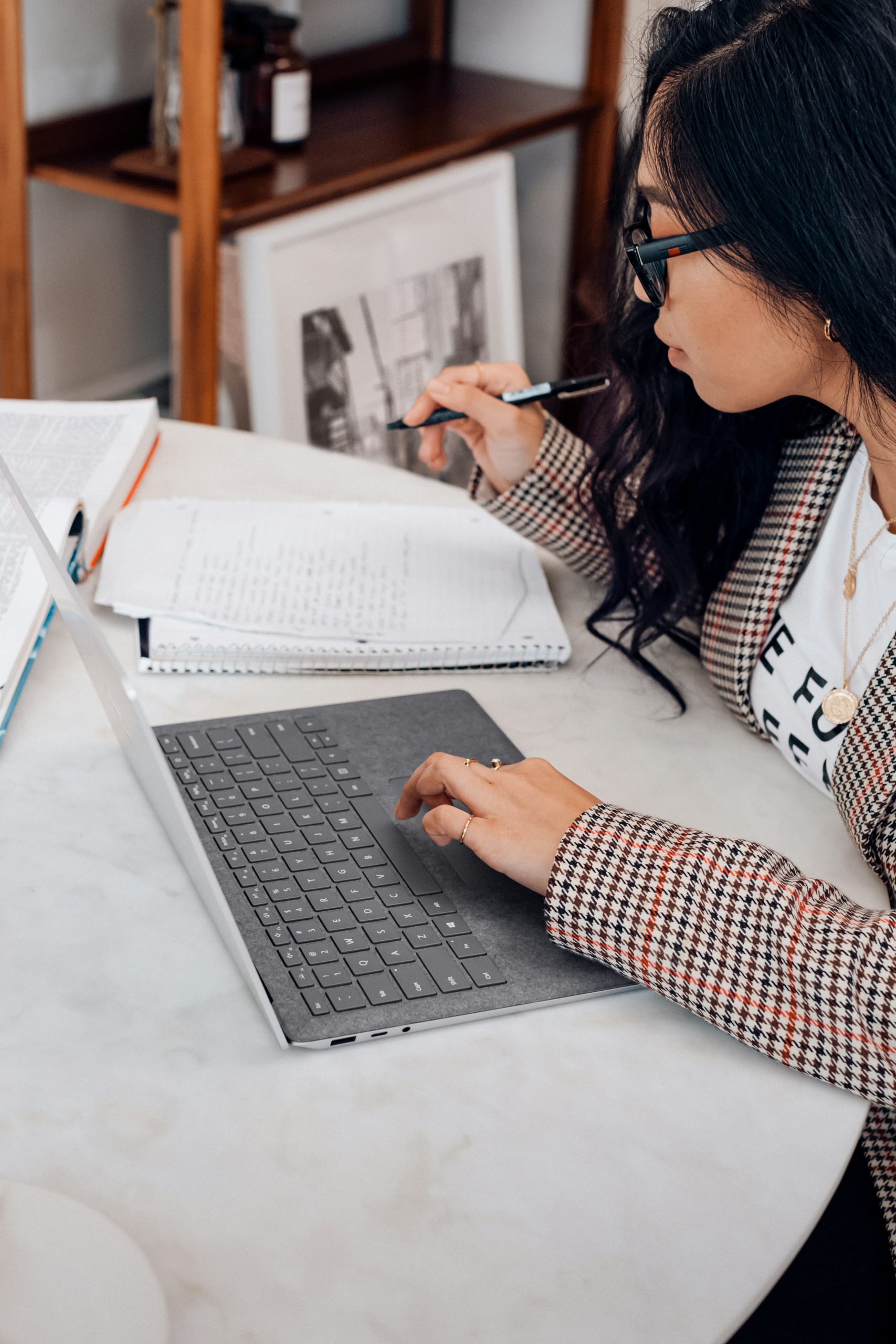 A person is seen working on a laptop while referring to a notebook.