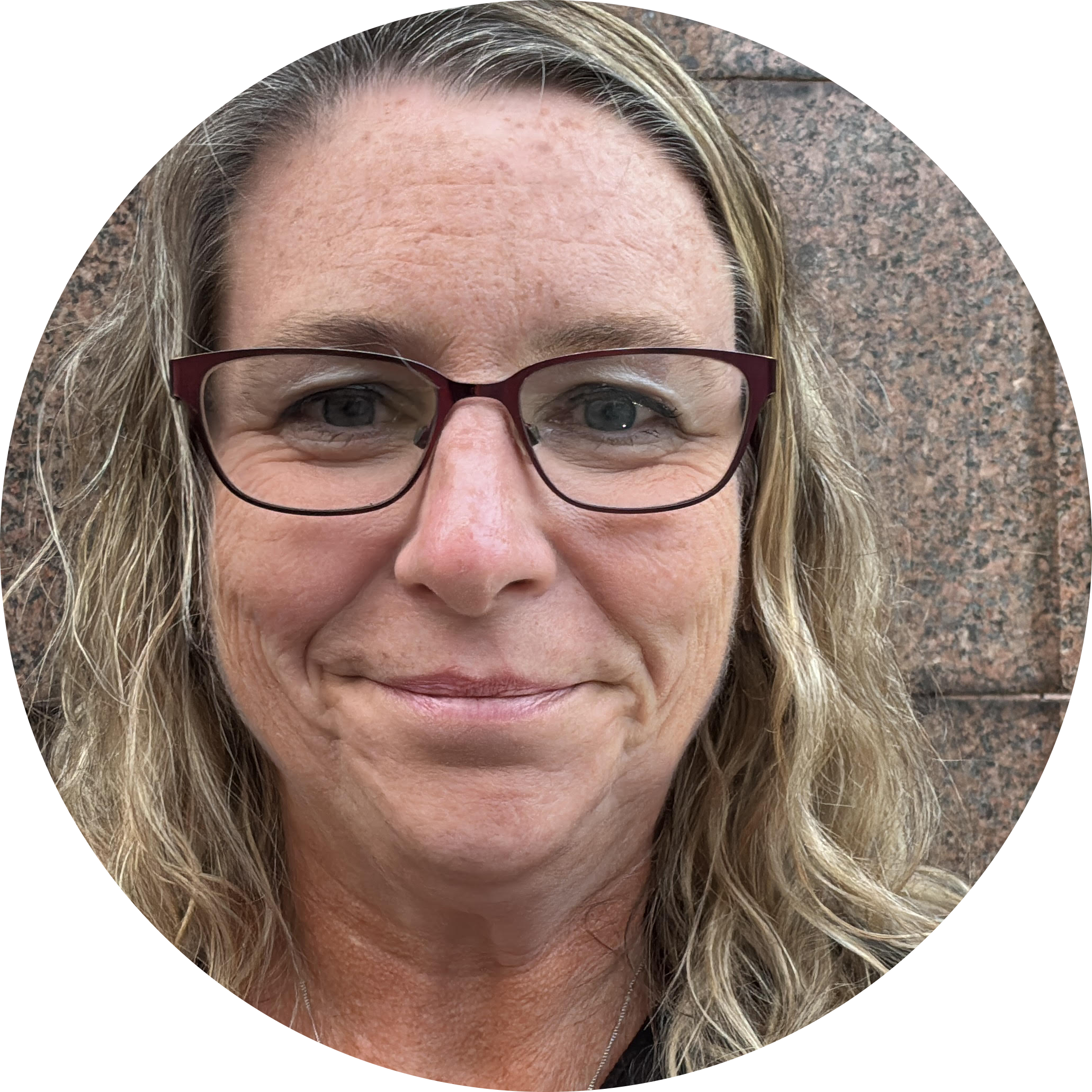 A woman with long, curly light hair is wearing purple glasses and smiling.