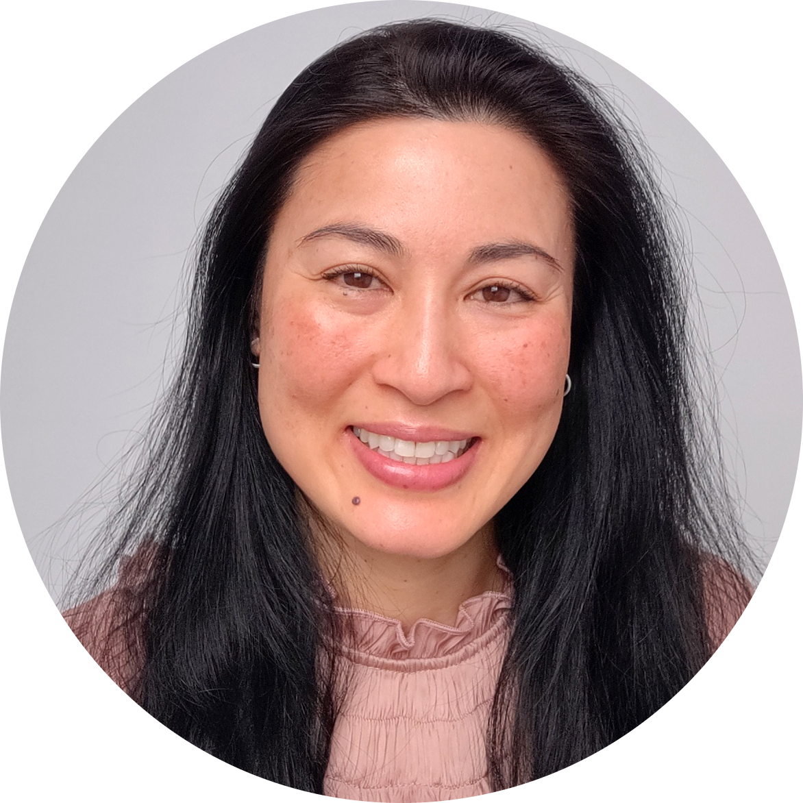 A smiling woman from Southeast Asia is wearing a light pink top and has long black hair.