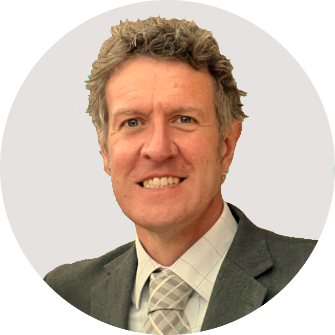 A tall white man with curly salt and pepper hair smiling dressed in a suit and tie.