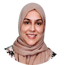 A smiling woman, wearing a beige head scarf (hijab) and a black/beige flowery shirt.