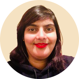 A smiling Pakistani woman with brown eyes and black shoulder-length hair wears bold red lip gloss.